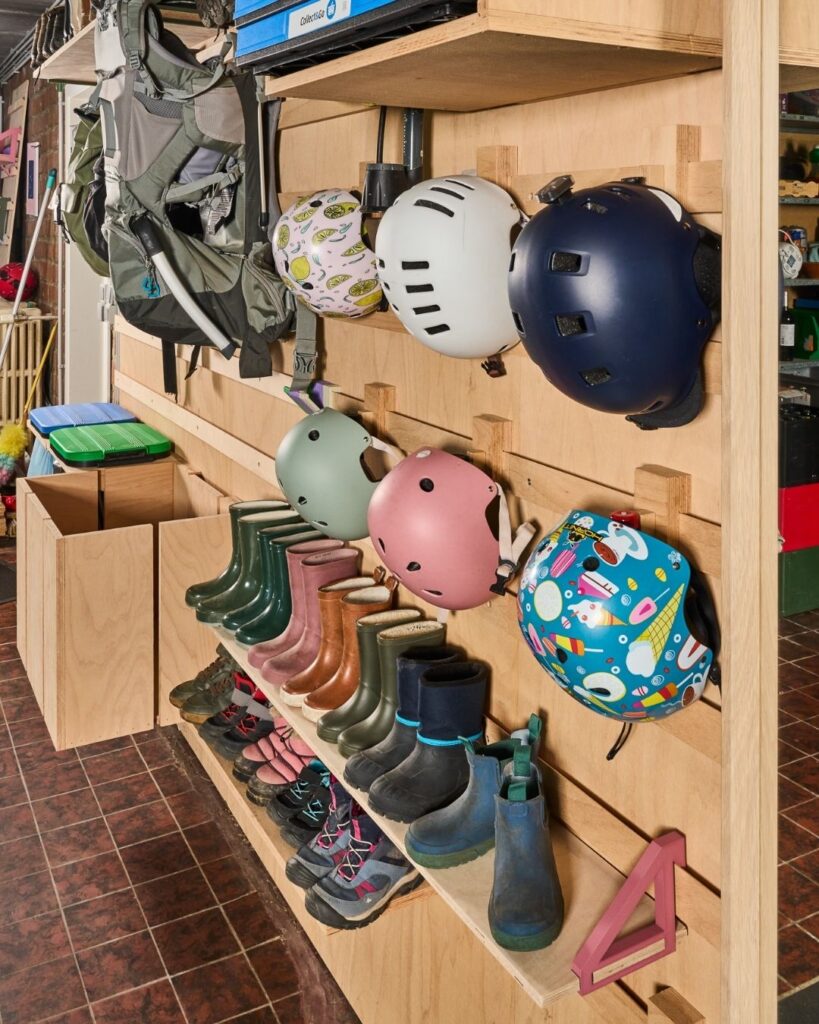 WandOrde modulair wandsysteem in garage met fietshelmen, kinderlaarzen, schoenen en buggy netjes opgeborgen aan de wand.