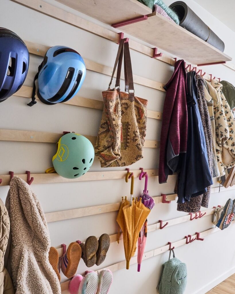 WandOrde modulair wandsysteem met roze haken voor jassen, fietshelmen, tassen, paraplu’s en kinderspullen in de inkomhal.