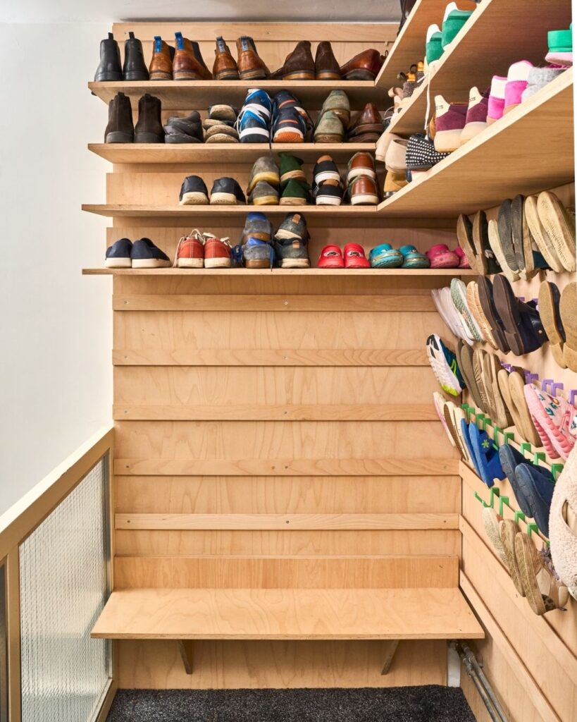 WandOrde schoenenopberging met houten legplanken en wandhaken voor kinderschoenen, volwassen schoenen en pantoffels in de inkomhal.