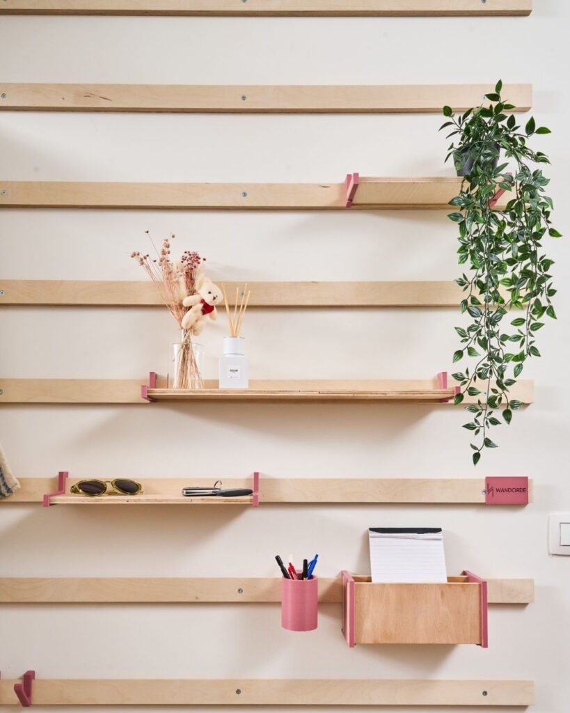 WandOrde modulair wandsysteem met roze accessoires, legplanken, plant, documenthouder en pennenpot voor leefruimte of bureauhoek.