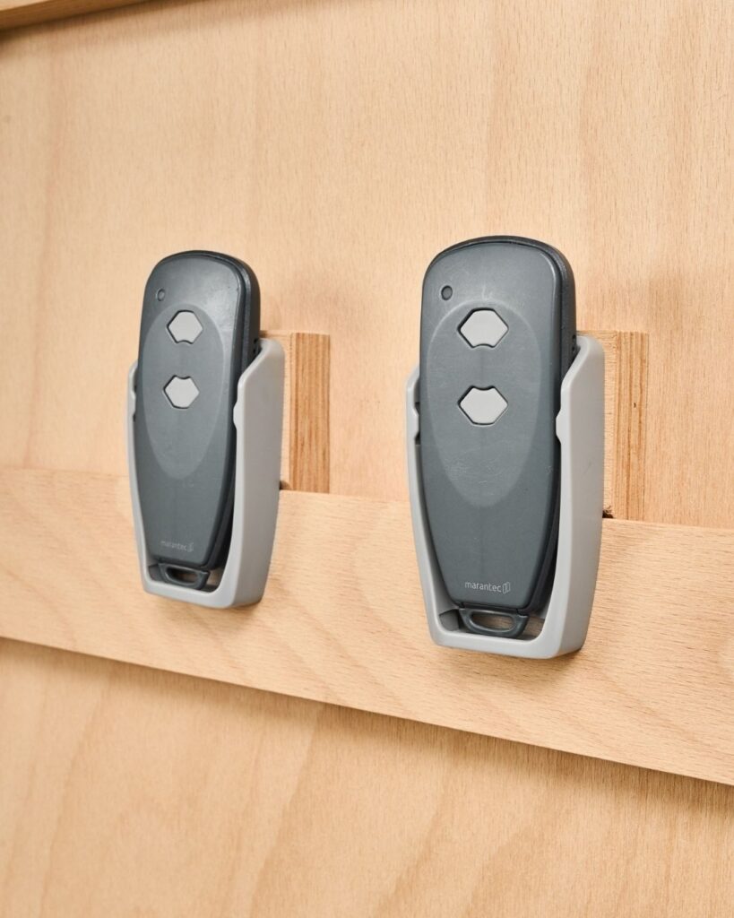 Twee afstandsbedieningen netjes opgeborgen in houders aan een houten WandOrde wandsysteem.
