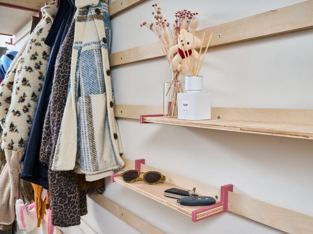 Modulair houten WandOrde wandsysteem met kapstok, roze legplanken, jassen, sleutels en decoratie in de inkomhal.
