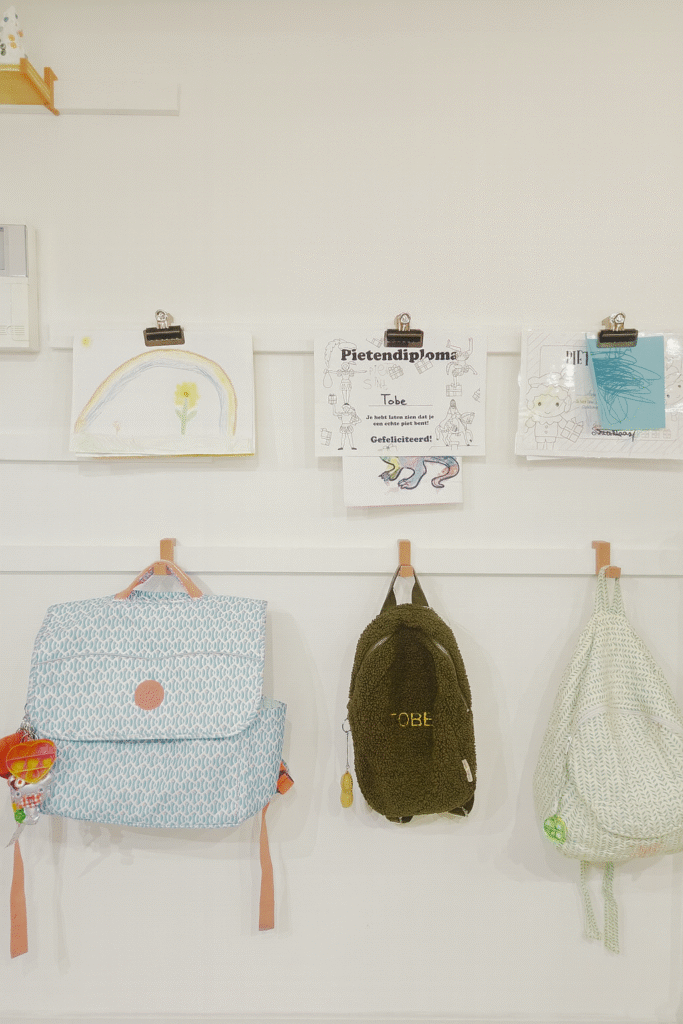 Modulair WandOrde-wandsysteem voor kinderen, met rugzakken en tekeningen netjes opgeborgen aan leren haken in de inkomhal