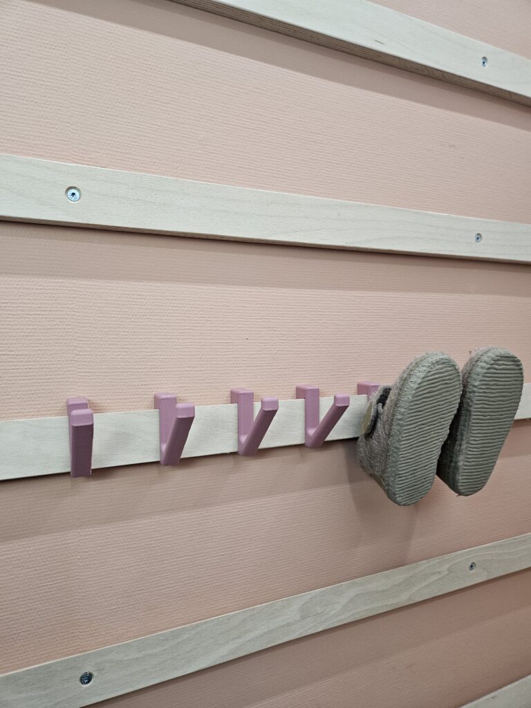 Modulair WandOrde wandsysteem met roze haakjes waarop kinderschoenen hangen, gemonteerd op houten lattenwand