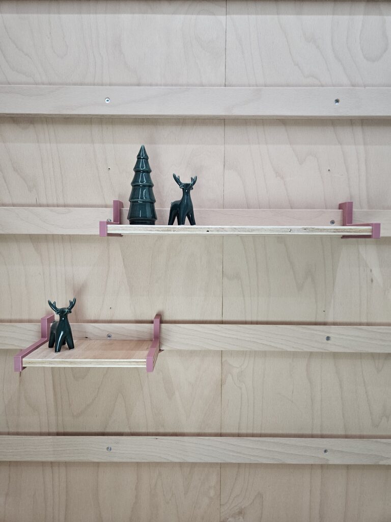 Modulair WandOrde wandsysteem met houten legplanken en roze metalen steunen, minimalistisch opgesteld met decoratieve objecten