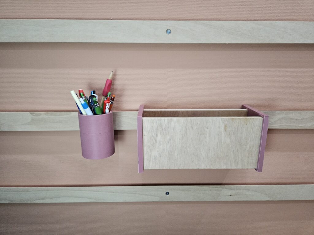 Modulair WandOrde wandsysteem met roze penhouder en houten boekenvak, gemonteerd op wand met houten latten